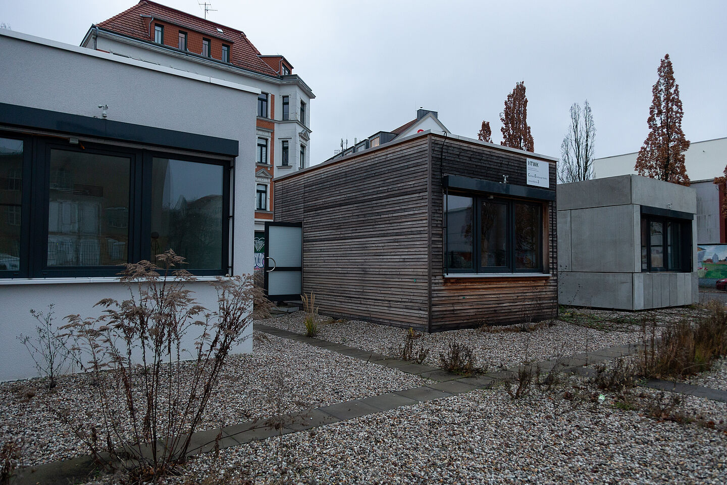 Drei Raummodule. Das ganz rechts hat eine Fassade aus Betonplatten, das Mittlere eine Holzfassade und das Linke ist weiß verputzt.