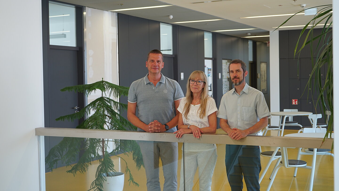Zuhause im Nieper-Bau: Prof. Gero Guzek (GG), Dagmar Fester (DF), Prof. Robert Huhn (RH). (v.l.) drei Personen an einem Geländer in modernem Innenraum