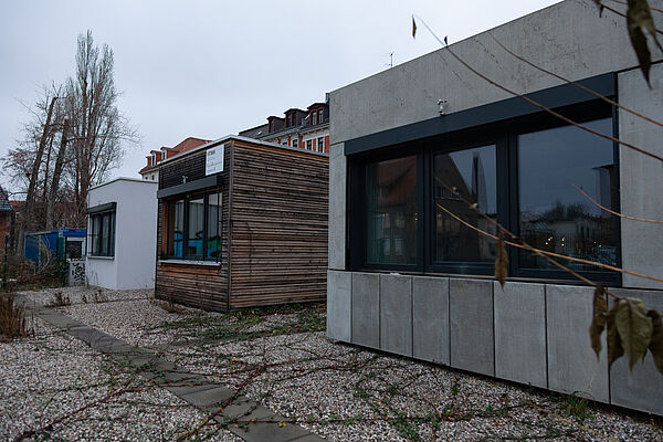 Drei Raummodule. Das ganz rechts hat eine Fassade aus Betonplatten, das Mittlere eine Holzfassade und das Linke ist weiß verputzt.