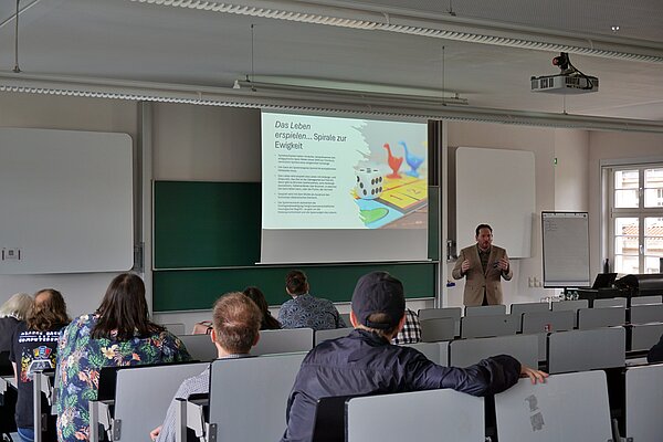 Dr. Manuel Stübecke bei seiner Präsentation zum Thema „Mensch, ärgere dich nicht!“ beim Science Mashup am 9. Mai. Im Hörsaal wird der Präsentation von Herrn Dr. Stübecke gelauscht.