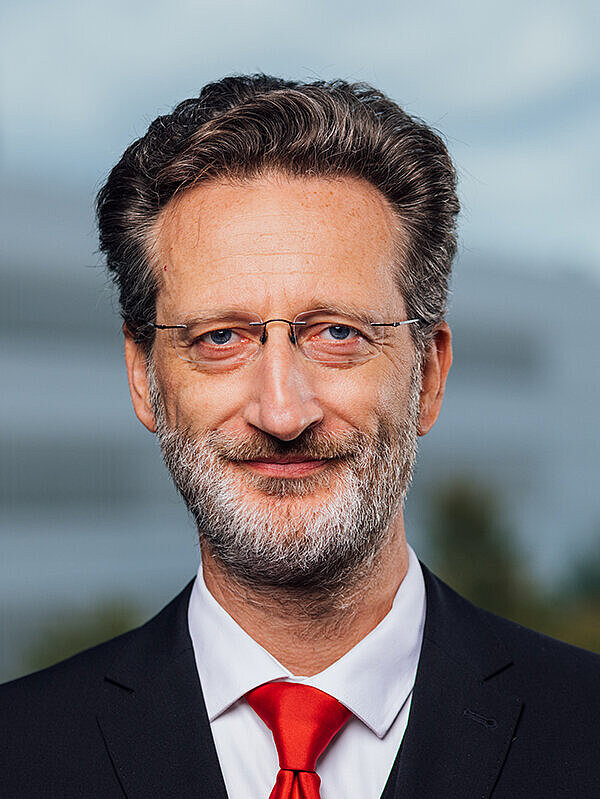 Portrait einer lächelnden Person vor einem Hochschulgebäude 